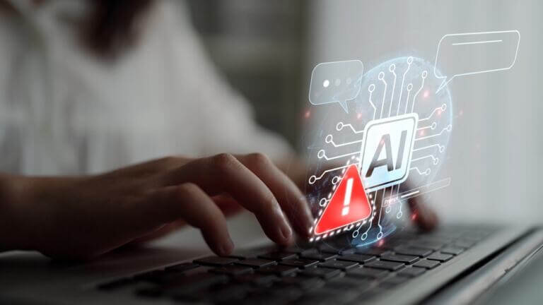 Manos escribiendo en una laptop con un ícono de advertencia y un gráfico que representa inteligencia artificial, destacando los riesgos de alucinaciones en IA.