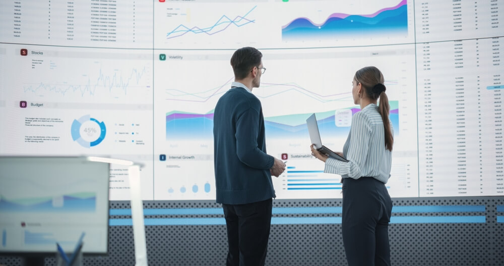 Dos profesionales analizan gráficos financieros y de datos en una sala de control digital, representando cómo Spark facilita el procesamiento de Big Data en tiempo real para empresas.